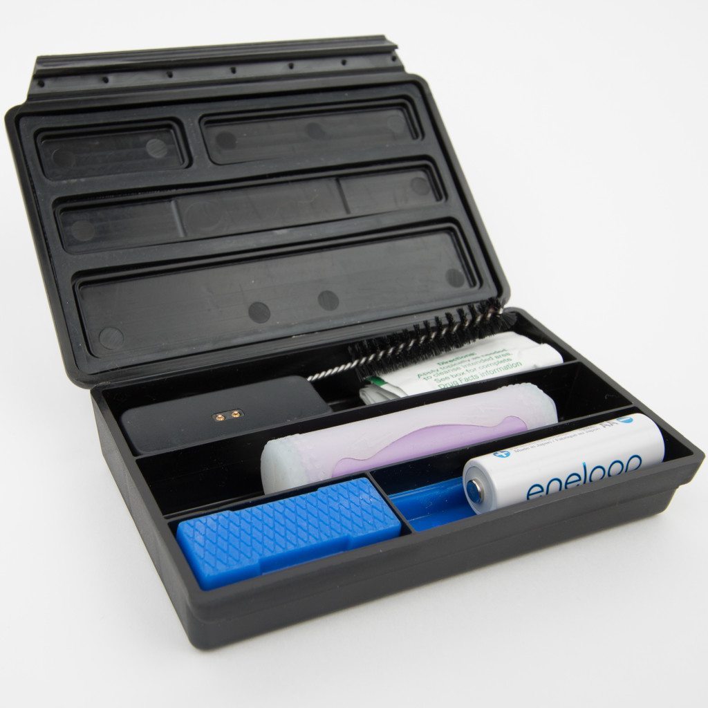 Bhanga Box open with Pax 2 charging block, alcohol wipes, cleaning brush, an 18650 battery, one AA battery, and a silicone insert in the smallest compartment